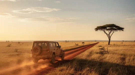 Véhicule 4x4 solitaire sur une piste de terre rouge traversant la savane africaine au lever du soleil