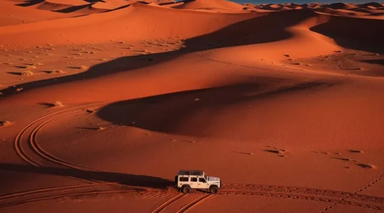 Vue aérienne d'un 4x4 traversant une dune immense de sable rouge dans le désert du Namib