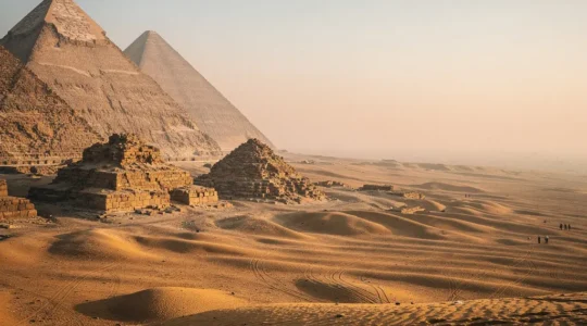 Vue panoramique des pyramides de Gizeh baignées par la lumière dorée de l'aube avec quelques visiteurs au loin