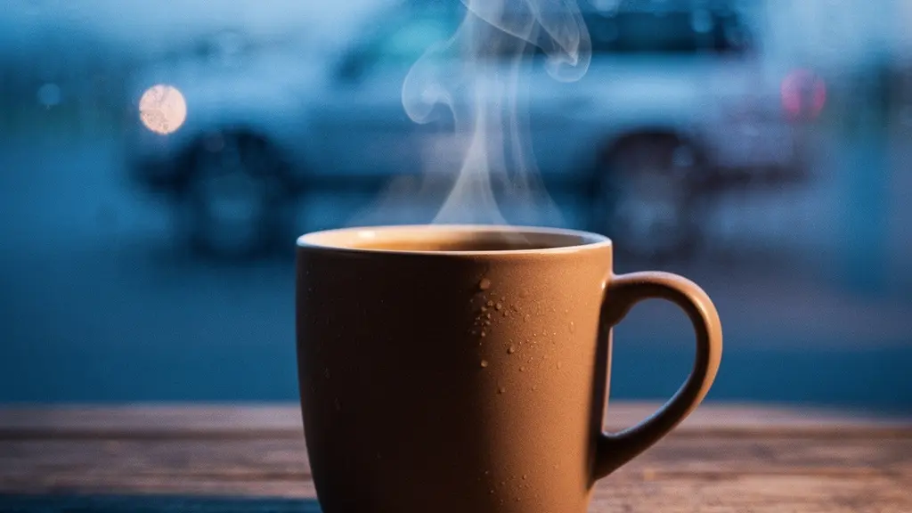 Gros plan sur une tasse de café fumante posée sur une surface en bois à l'aube, avec un reflet de véhicule de voyage en arrière-plan flou